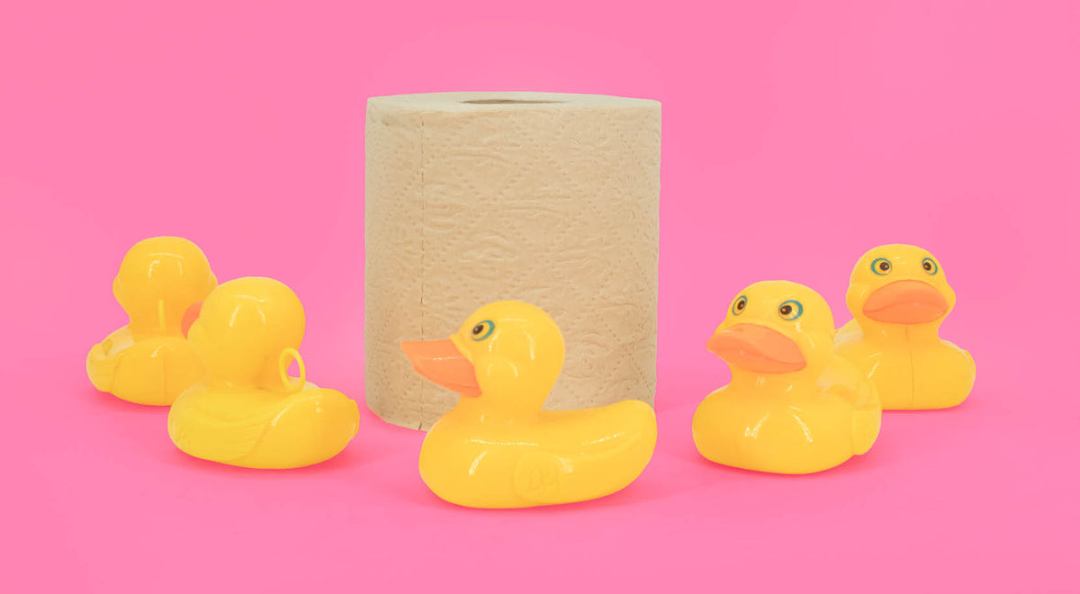 Four yellow rubber ducks and a roll of bamboo bobbi toilet roll on a pink background