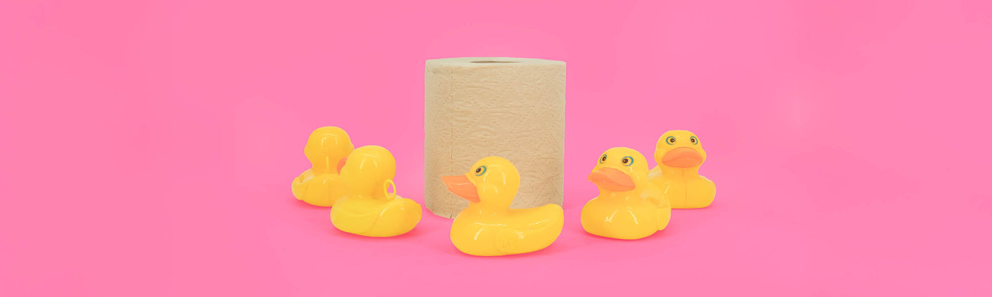 Four yellow rubber ducks and a roll of bamboo bobbi toilet roll on a pink background